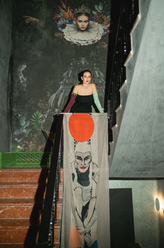 Ana Sneeringer standing on the steps showing her long scarf in gray color with female portrait as design